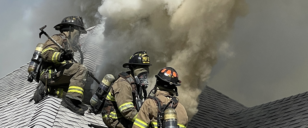 Firemen on roof of house that's on fire.