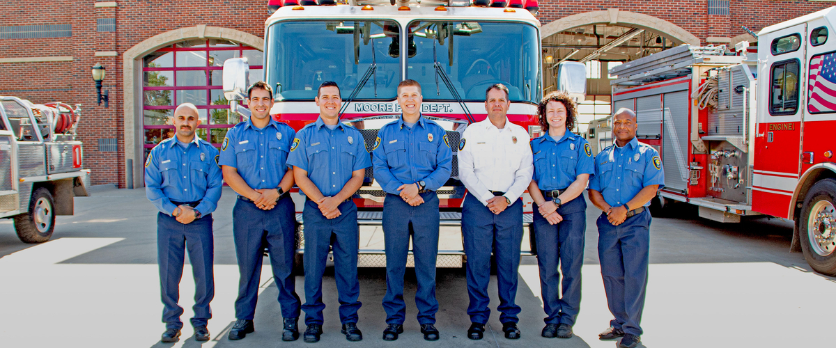 Line of firemen in front of fire truck.